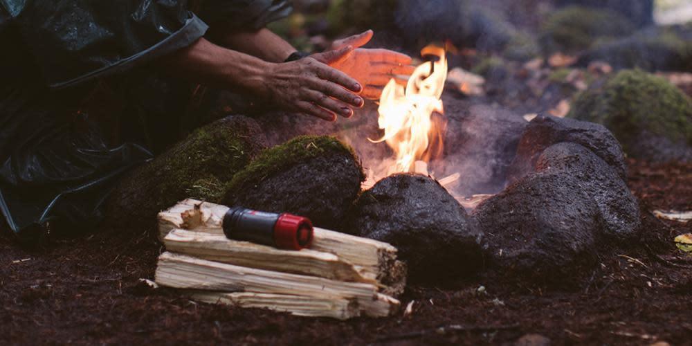 Person warming hands by a campfire with Zippo Typhoon Match Kit on firewood outdoors