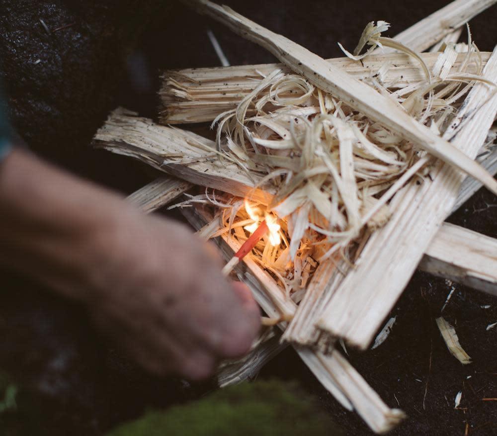 Hand lighting kindling stack outdoors with Zippo Typhoon match for camping fire